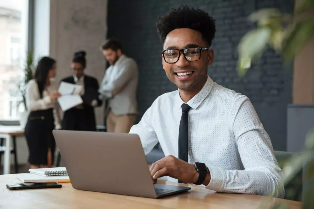 Jovem advogado, sorridente, mexendo em seu laptop, em escritório de advocacia no topo da tecnologia