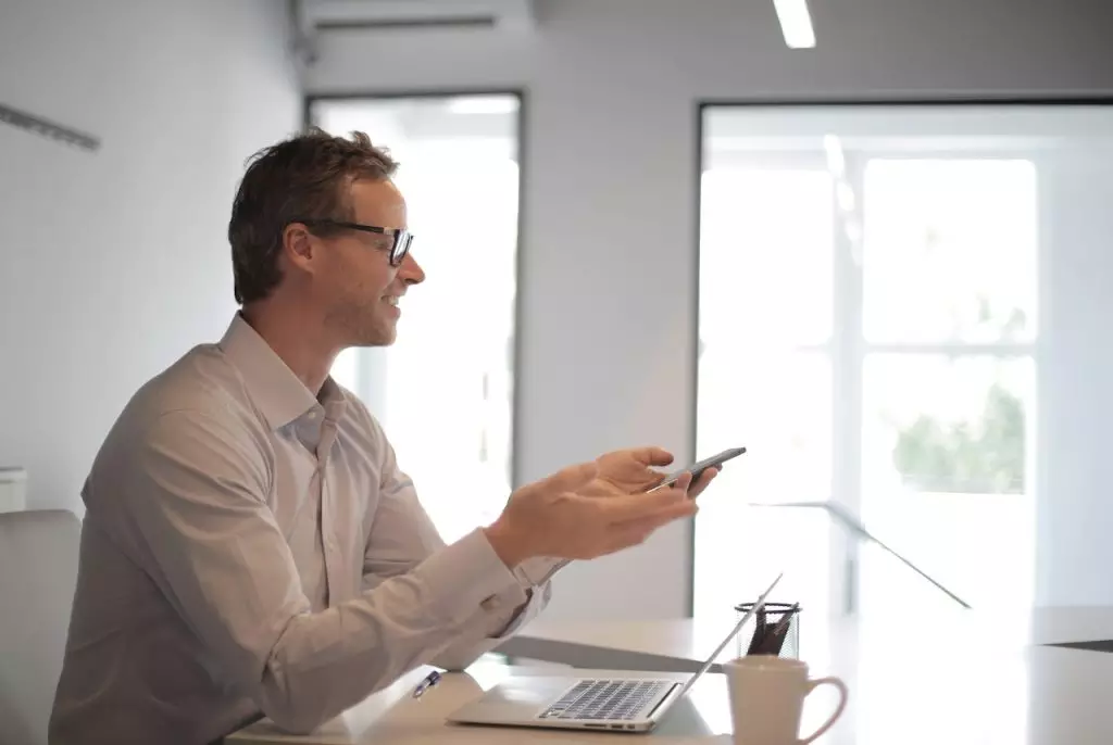 Homem, sentado, com notebook na mesa e celular à mão, utilizando sistema para advogados